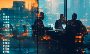 Team of professionals in a glass-walled conference room at night, laptops open, city lights reflected on the windows.