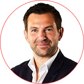 Professional headshot of a smiling man in a dark blazer and white shirt against a white background, circular crop with a red border.