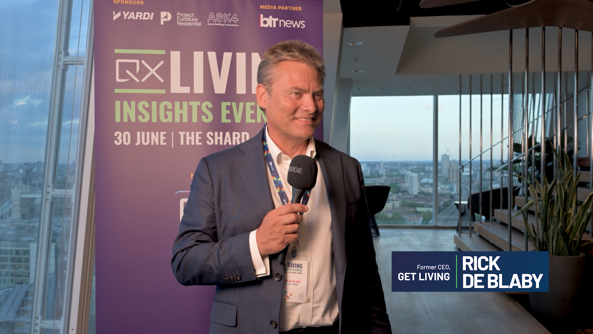 Man in a suit being interviewed with a handheld microphone at a 'Live Insights Event' backdrop in a modern venue overlooking the city.