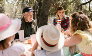 Group of people wearing hats enjoying an outdoor picnic at a sunny backyard table.