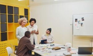 Four colleagues collaborate around a table in a bright office, with yellow storage units in the background.