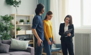 A woman in a blazer showing a clipboard to a couple in a bright living room, discussing documents.